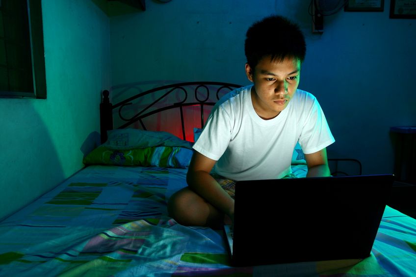 Adolescent devant son écran d'ordinateur sur son lit la nuit